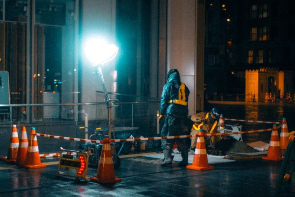 Construction workers at night in a city with bright lights and reflections.