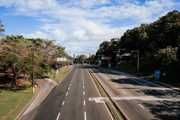 An empty highway lined with greenery, captured in clear daylight under blue skies.